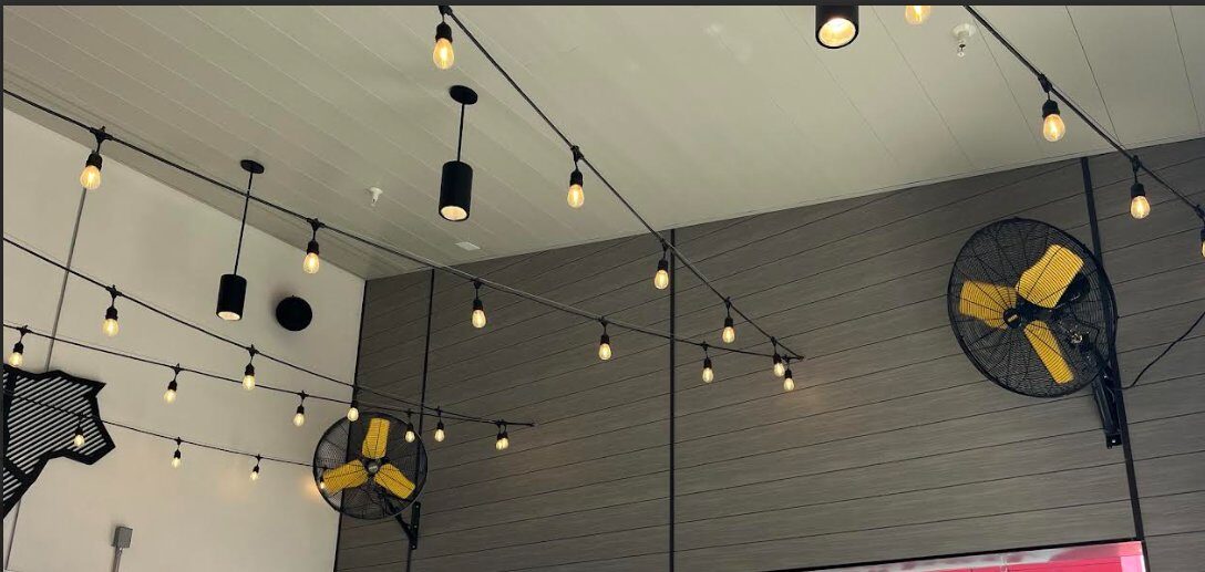 Commercial pendant and string light installation across high-ceiling restaurant dining area with circulation fans