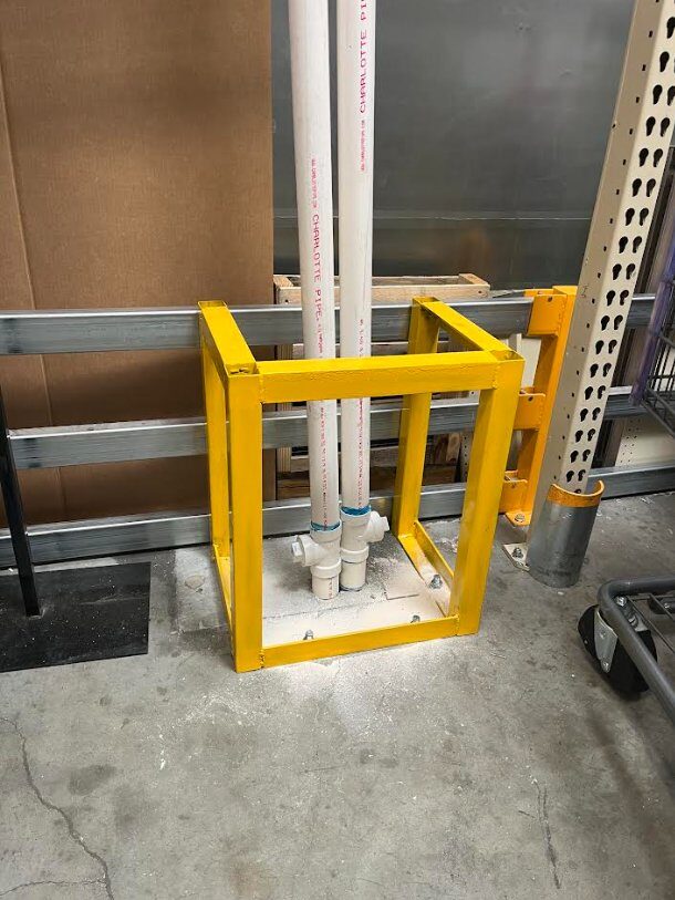 Custom-fabricated safety-yellow steel barrier cage protecting PVC supply lines, installed by FST