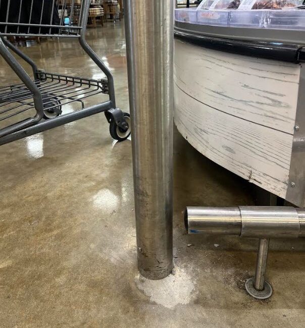 Interior stainless steel bollard installed to protect refrigerated display case from shopping cart impact damage