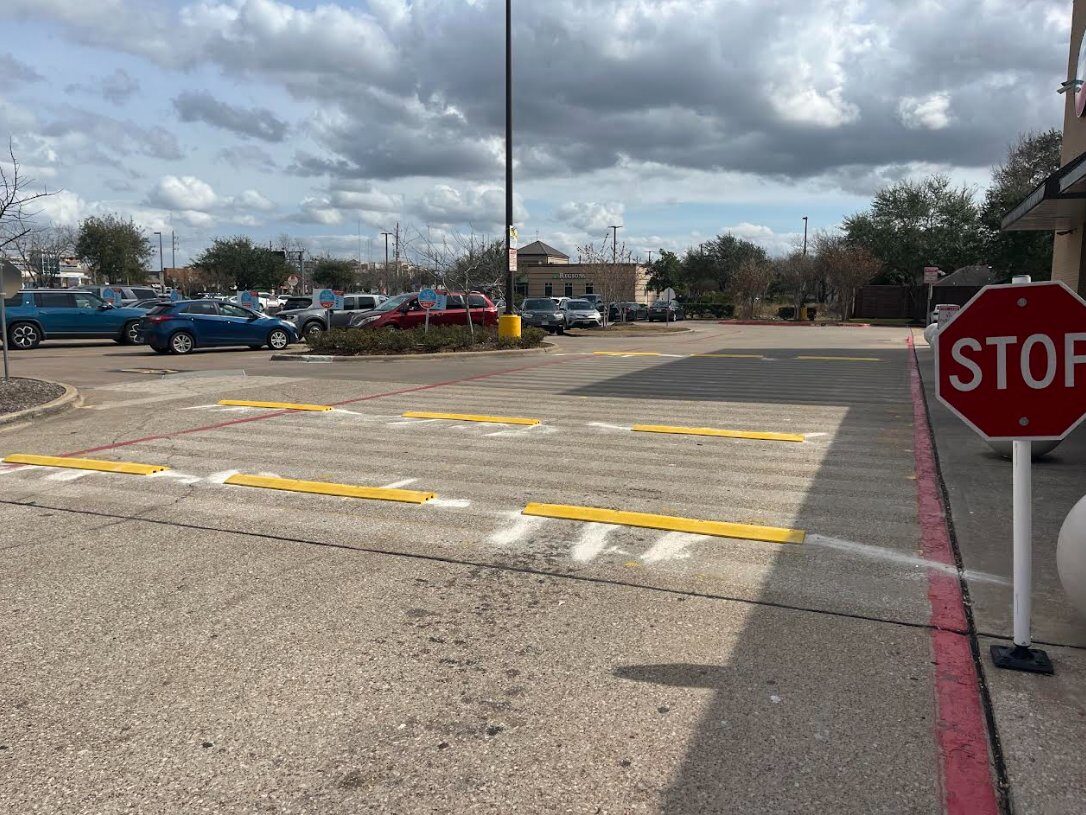 Houston retail center parking lot with fresh yellow speed bump installation and red curb restriping by FST