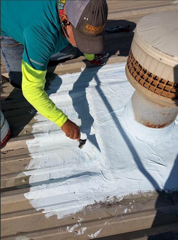 FST technician hand-applying sealant around a roof vent penetration on a commercial standing-seam metal roof, Houston metro