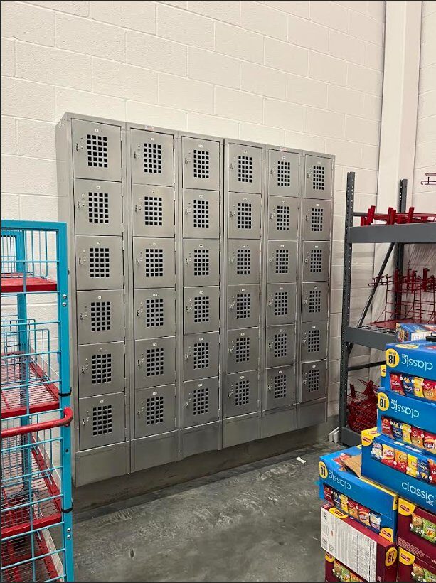 36-unit stainless steel employee locker bank installed against CMU wall in grocery back-of-house staff area, plumb and aligned