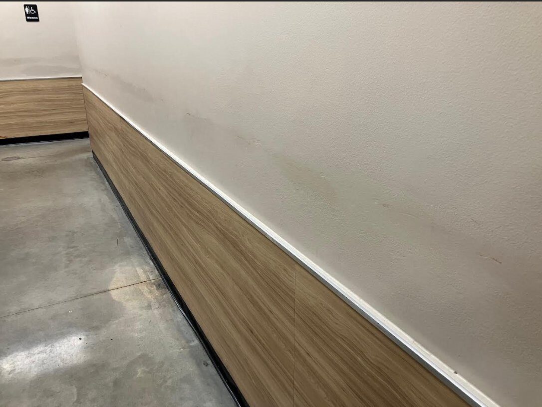 Wall protection paneling installation in progress along a retail back-of-house corridor — wood-grain rigid impact panels